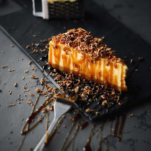 A piece of cheesecake covered in caramel and chocolate flakes.