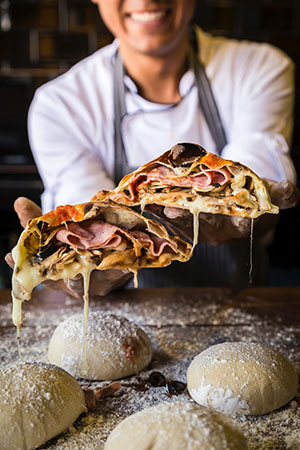 The founder of Food Guru is showing a gooey meat and cheese sandwich on top of raw dough balls dusted with flour.