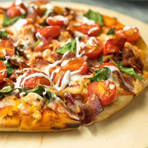 A pizza topped with pieces of tomato, basil, and a drizzle of ranch.