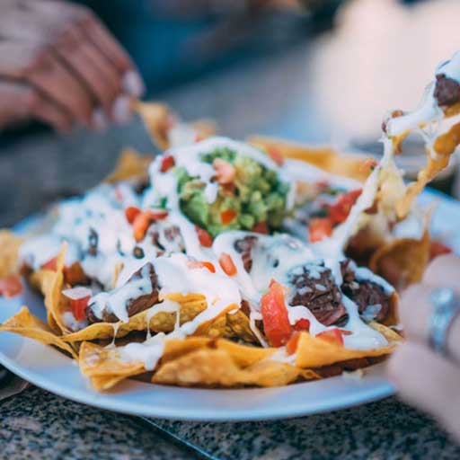 People sharing a plate of loaded nachos with guacamole.